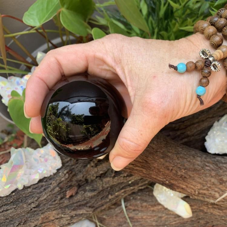 A polished black obsidian sphere held in one hand, its glossy surface reflecting the garden around it