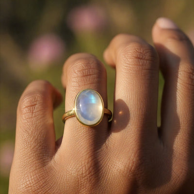The moonstone and gold ring worn on a finger, its stone flashing soft blue in warm light