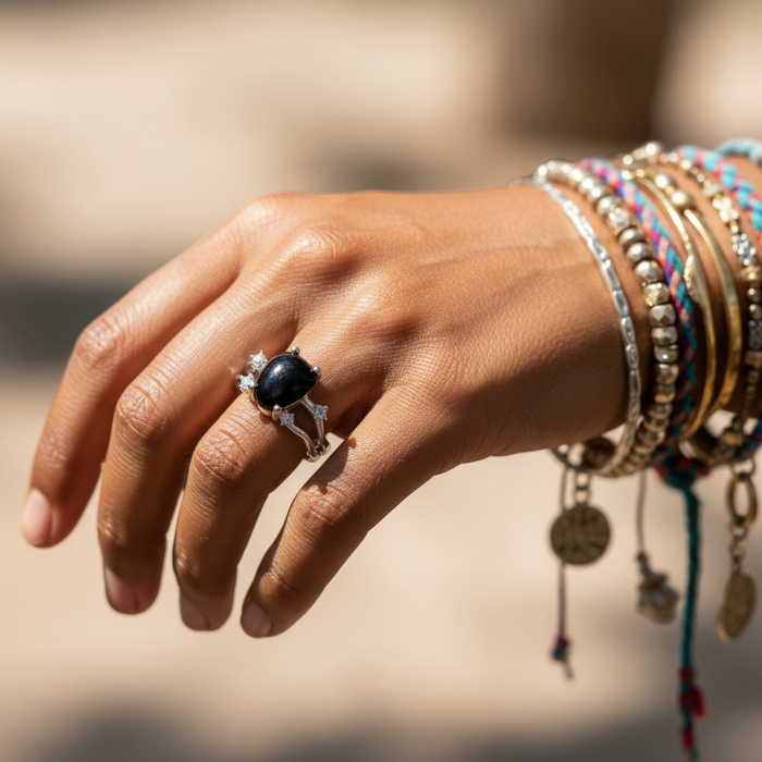 The black onyx and silver ring worn on a hand beside a stack of beaded bracelets