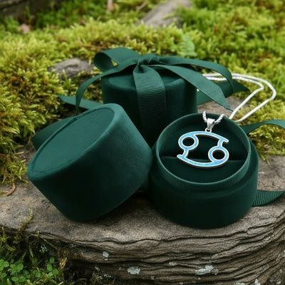 The Cancer opal pendant resting in an open round green velvet jewelry box on a mossy stone