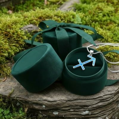The Sagittarius opal pendant resting in an open round green velvet jewelry box on a mossy stone