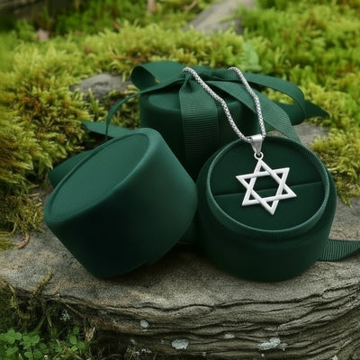 The silver Star of David pendant resting in an open round green velvet jewelry box on a mossy stone