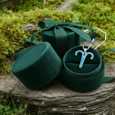The Aries opal pendant resting in an open round green velvet jewelry box on a mossy stone