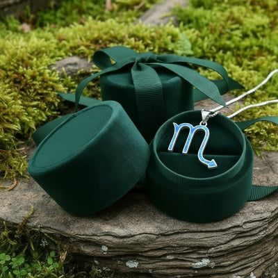 The Scorpio opal pendant resting in an open round green velvet jewelry box on moss