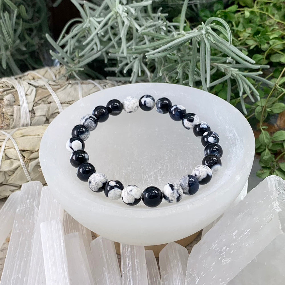 Orca Jasper bead bracelet in glossy black and white-splashed beads resting in a white selenite bowl