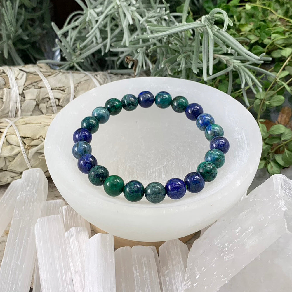 One azurite mala bracelet of round deep blue and green beads resting in a white selenite bowl