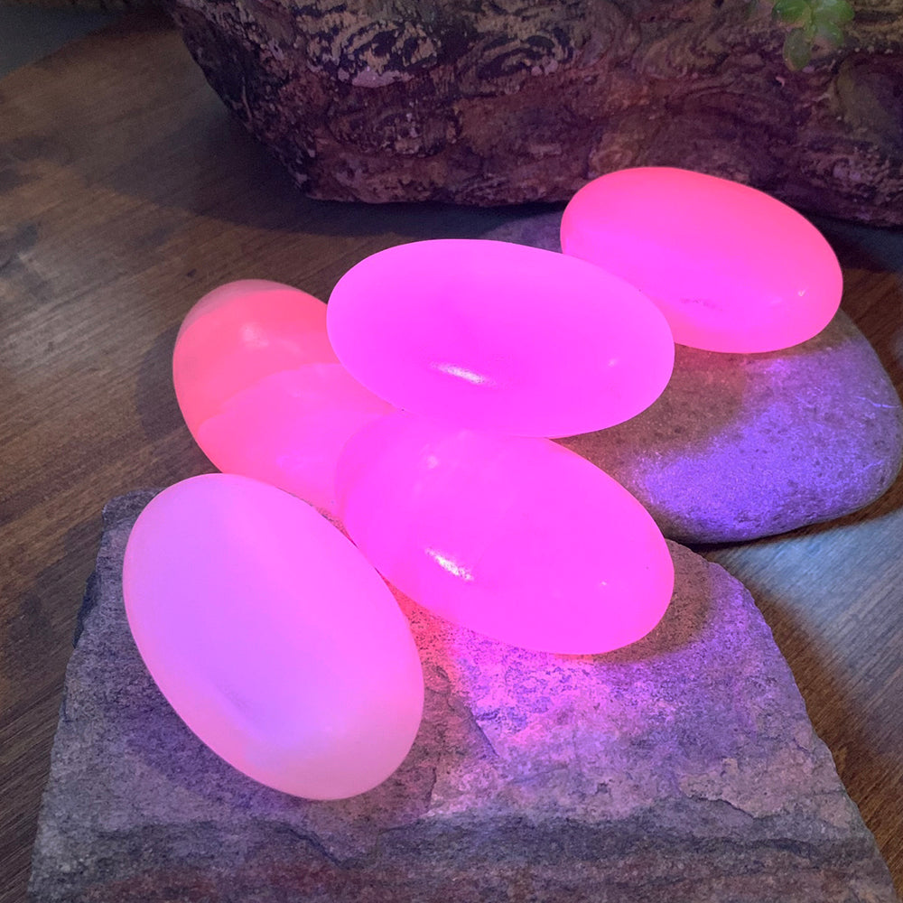 Several pink calcite palmstones glowing bright pink under ultraviolet light on dark stones