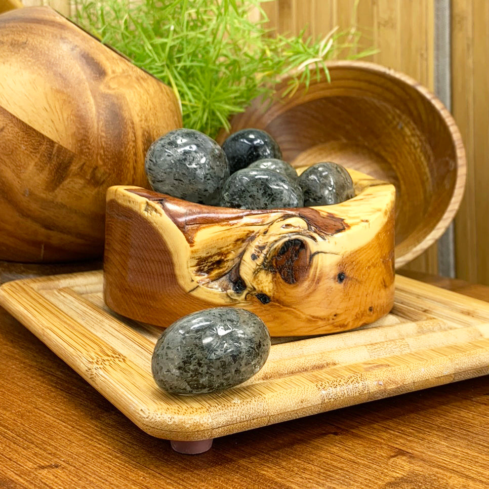 Polished kiwi jasper tumbled stones in a carved wooden bowl, with one ellipse stone resting in front on a bamboo tray