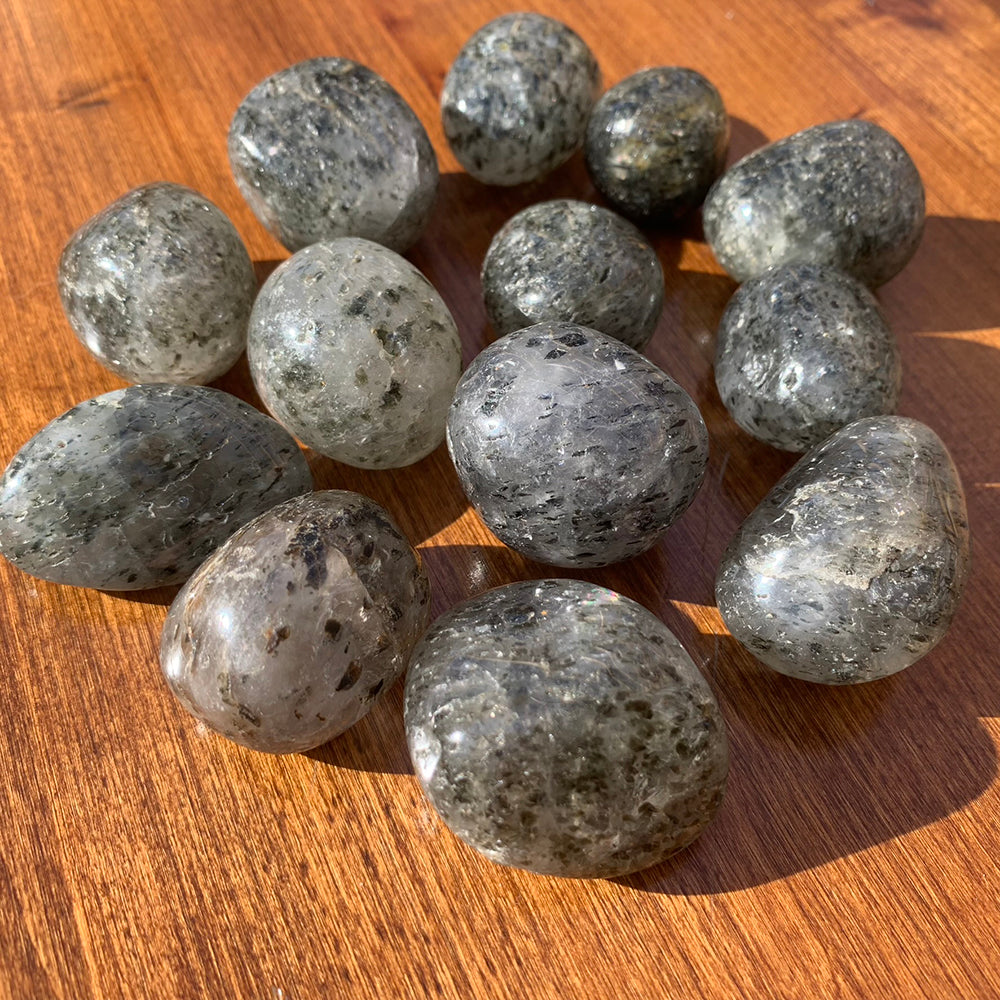 Close-up of a dozen kiwi jasper tumbled stones on a wooden table, showing soft green tones and dark mineral speckles