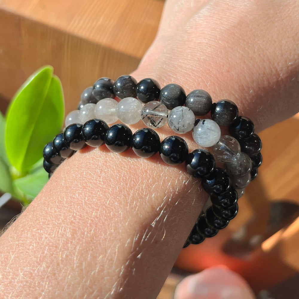 All three bead bracelets stacked on a wrist: black obsidian, black tourmalinated quartz and silver obsidian