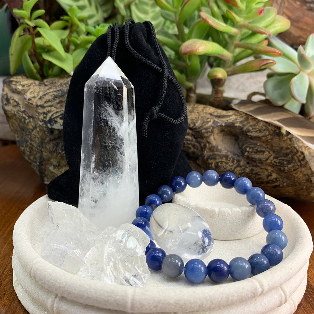 Clear quartz point, two rough quartz pieces, a clear quartz ellipse stone and a blue aventurine mala bracelet in a stone dish, with a black velvet pouch behind