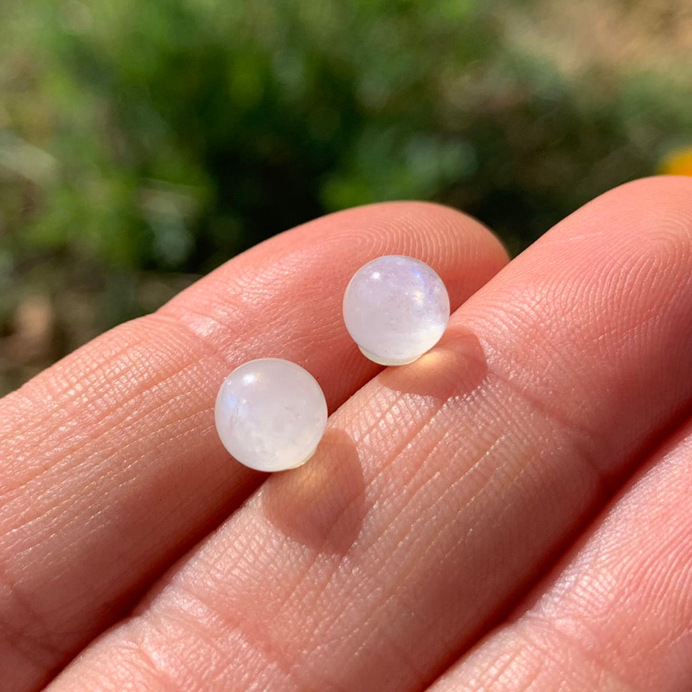 Two round, polished milky white quartz studs resting on fingertips in sunlight