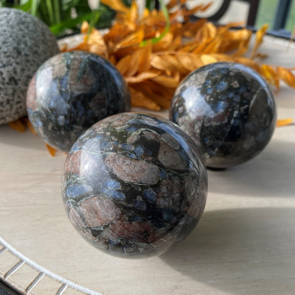Three polished que sera spheres in deep green-black with patches of dusty pink and bright blue, each with its own pattern