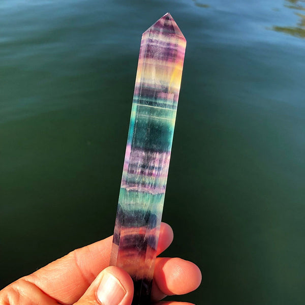 The rainbow fluorite point held up in one hand over open water