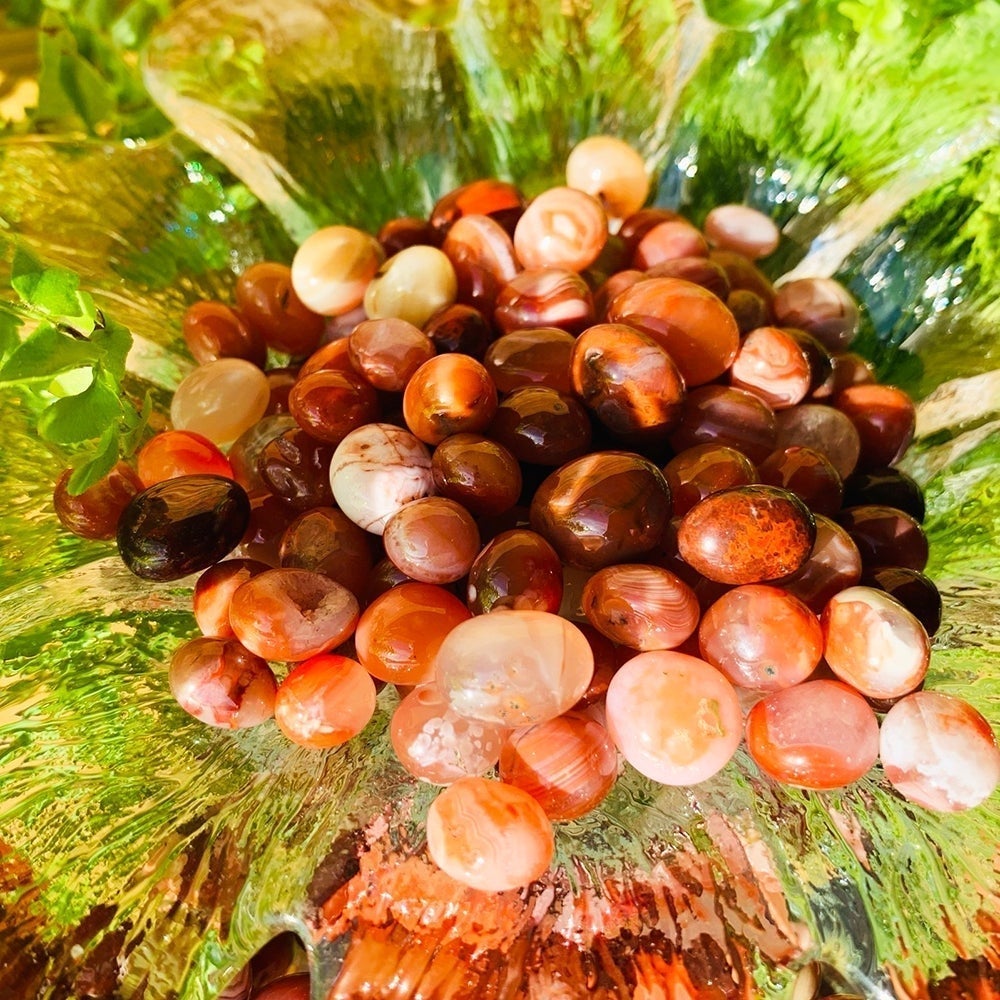 A heap of tumbled red carnelian mini gemstones in shades of orange, red, peach and cream, glowing in the light