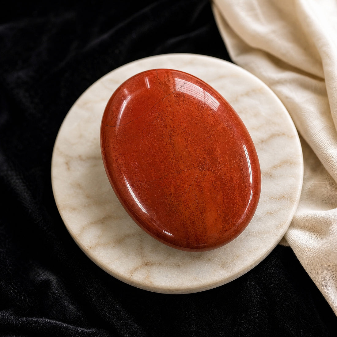 A glossy brick-red jasper palmstone with darker red banding on a pale marble dish