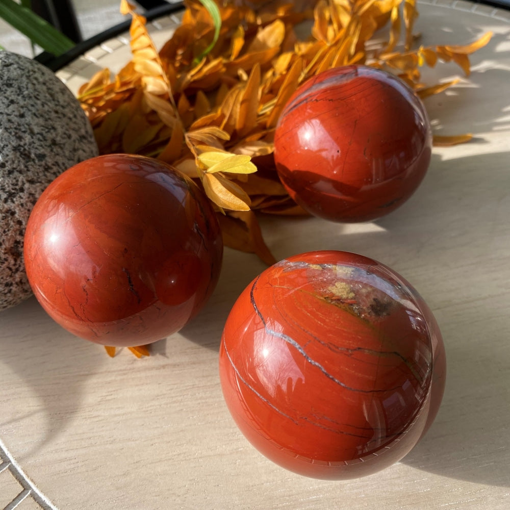 Three polished red jasper spheres on a pale wooden table, each with its own dark veins and lighter markings