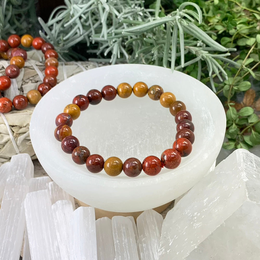 A single red earth mookaite jasper mala bracelet of round brick red, burgundy and mustard gold beads resting in a selenite bowl