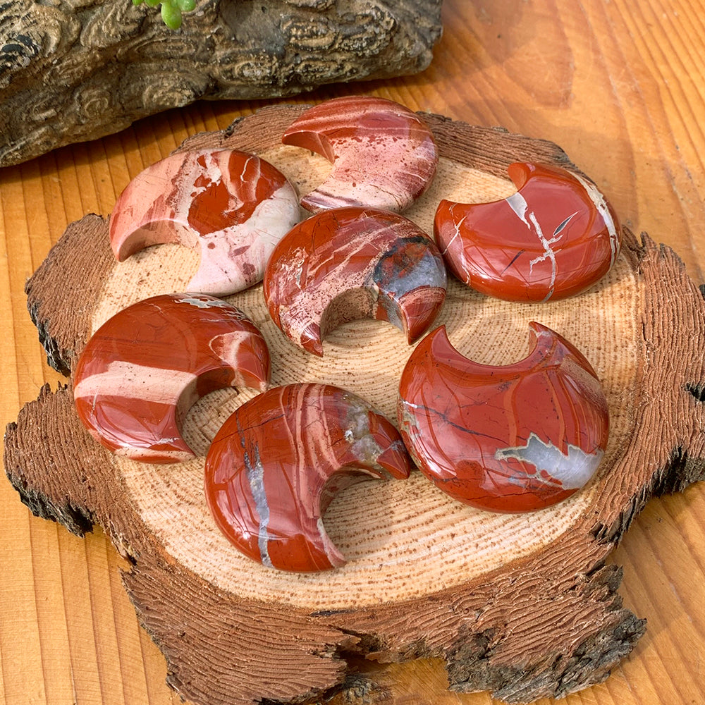 Seven red jasper crescent moons on a wood slab, each with its own swirl of red, cream and white