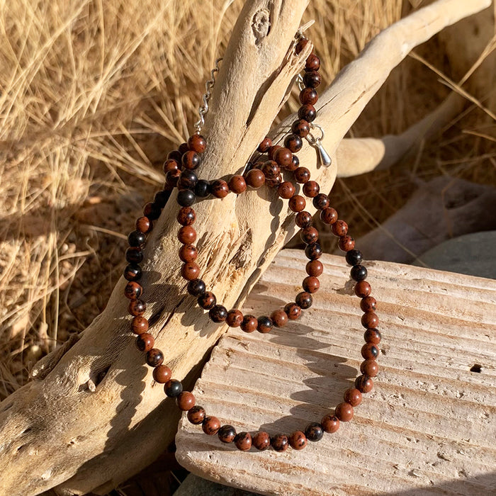 A strand of small red obsidian beads with a silver clasp draped over driftwood