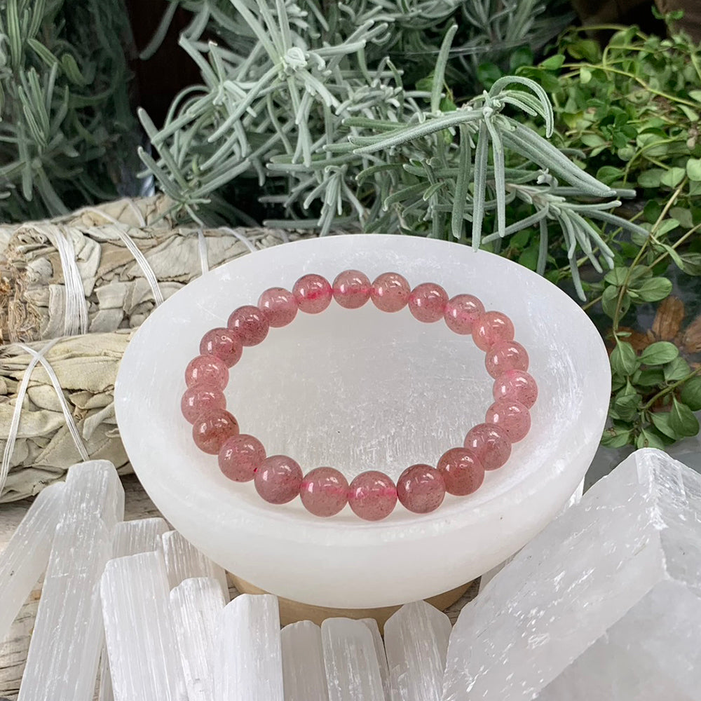 Strawberry quartz mala bracelet of translucent pink beads with fine red speckles resting in a selenite bowl