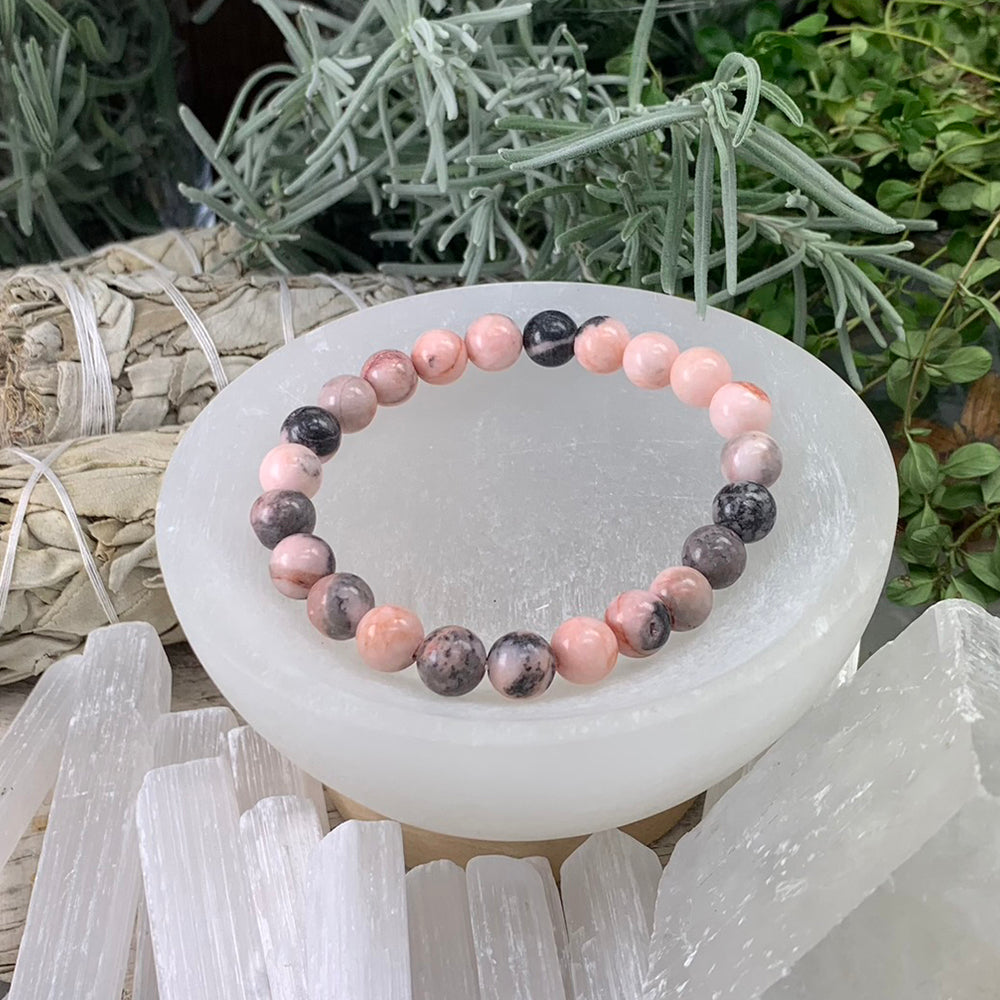 Red Zebra Jasper bead bracelet in soft coral pink and smoky grey beads resting in a white selenite bowl