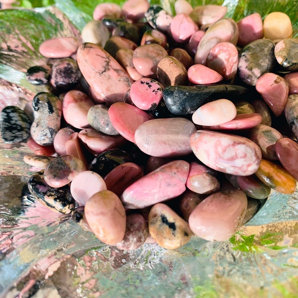 A heap of polished rhodonite mini gemstones in rose pink, blush and charcoal, with black veining