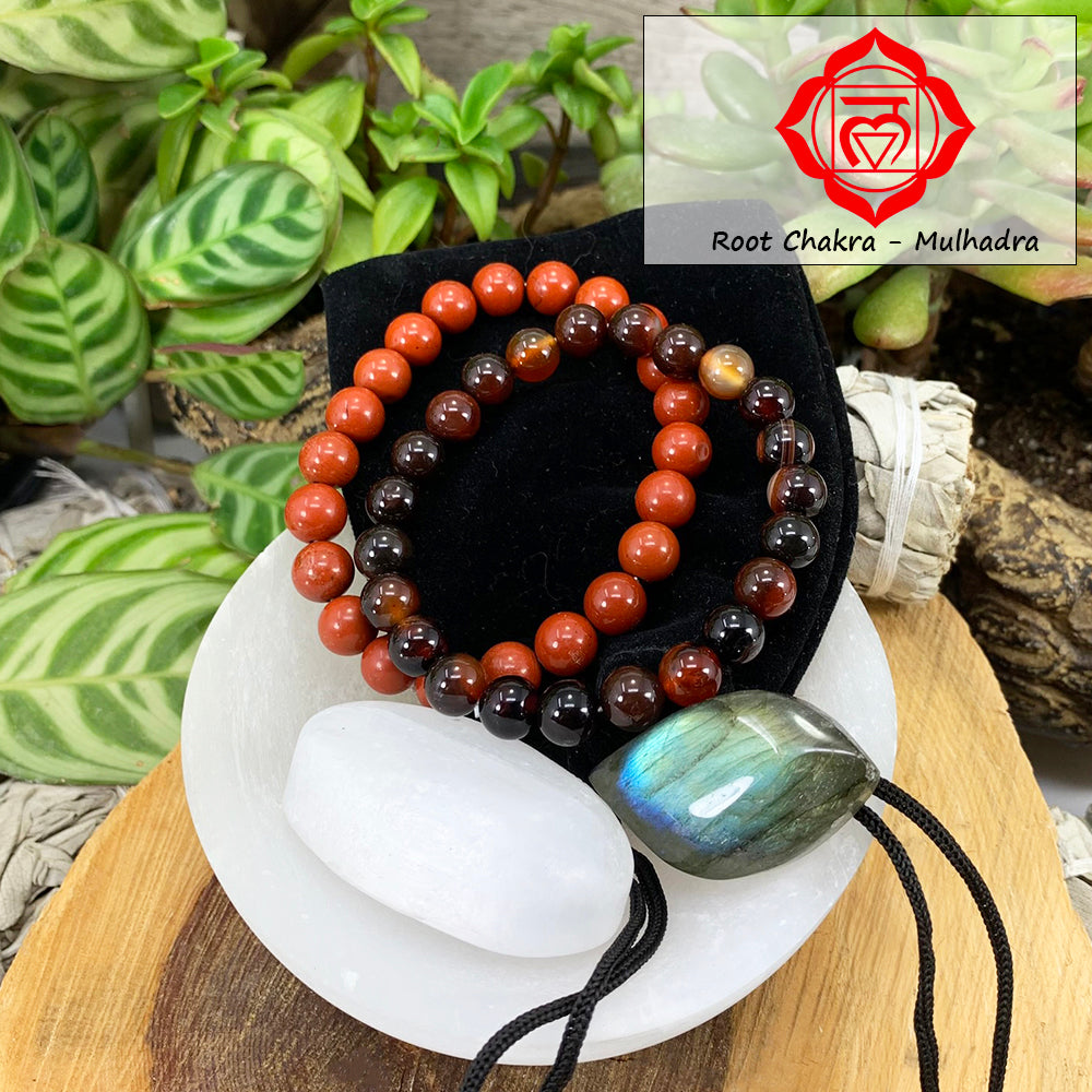Red jasper and black stripe agate mala bracelets on a black velvet pouch with a white selenite ellipse and a blue-flashing labradorite cabochon, in a selenite bowl