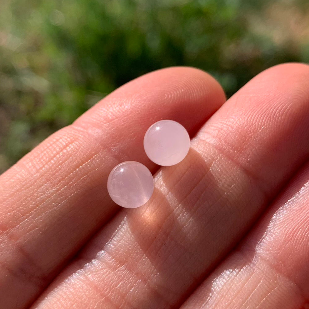Two round polished rose quartz studs resting on fingertips in sunlight