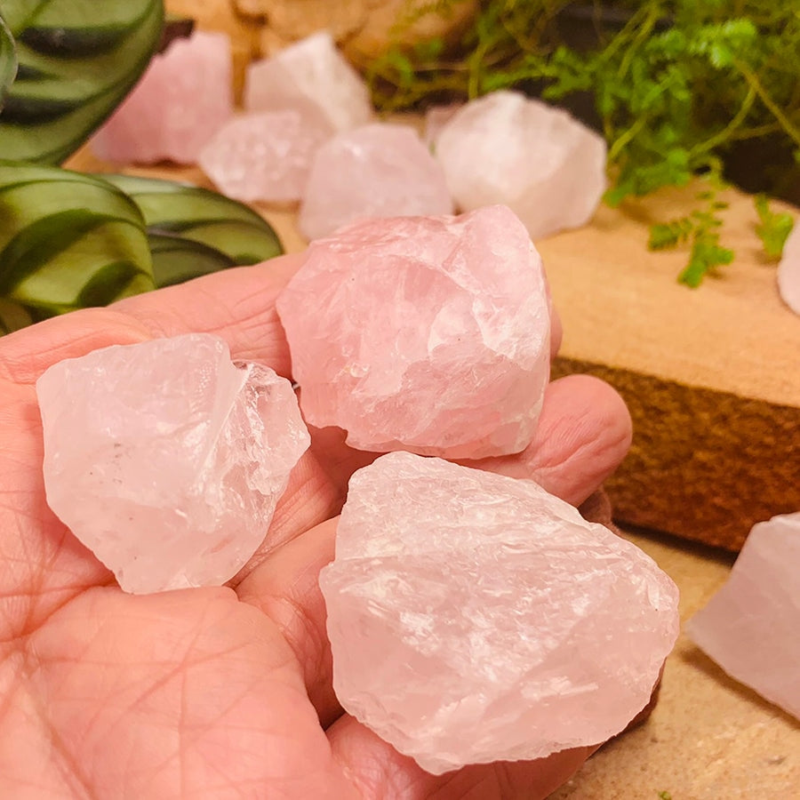 Rough pink rose quartz pieces resting in an open palm, with more pieces on a wooden board behind