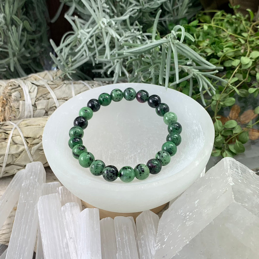 One ruby zoisite mala bracelet of round green beads with black flecks and touches of ruby pink, resting in a white selenite bowl