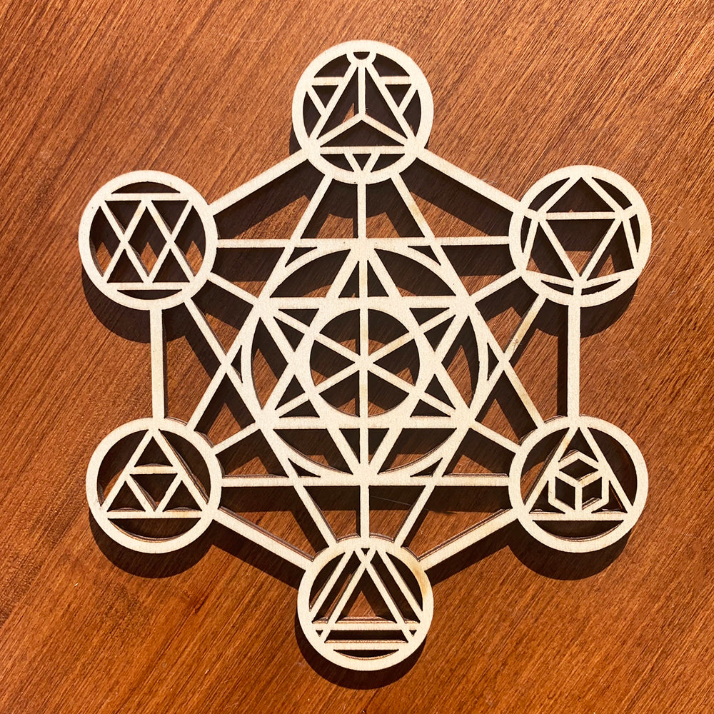 A pale laser-cut wooden sacred geometry grid of interlocking circles, lines and triangles, lying flat on a wooden table