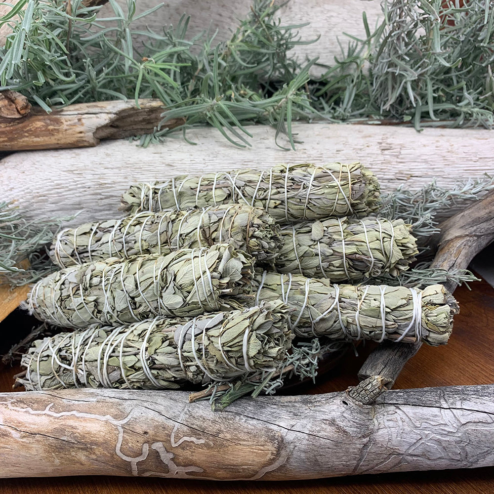 Six sage bundles stacked together on driftwood