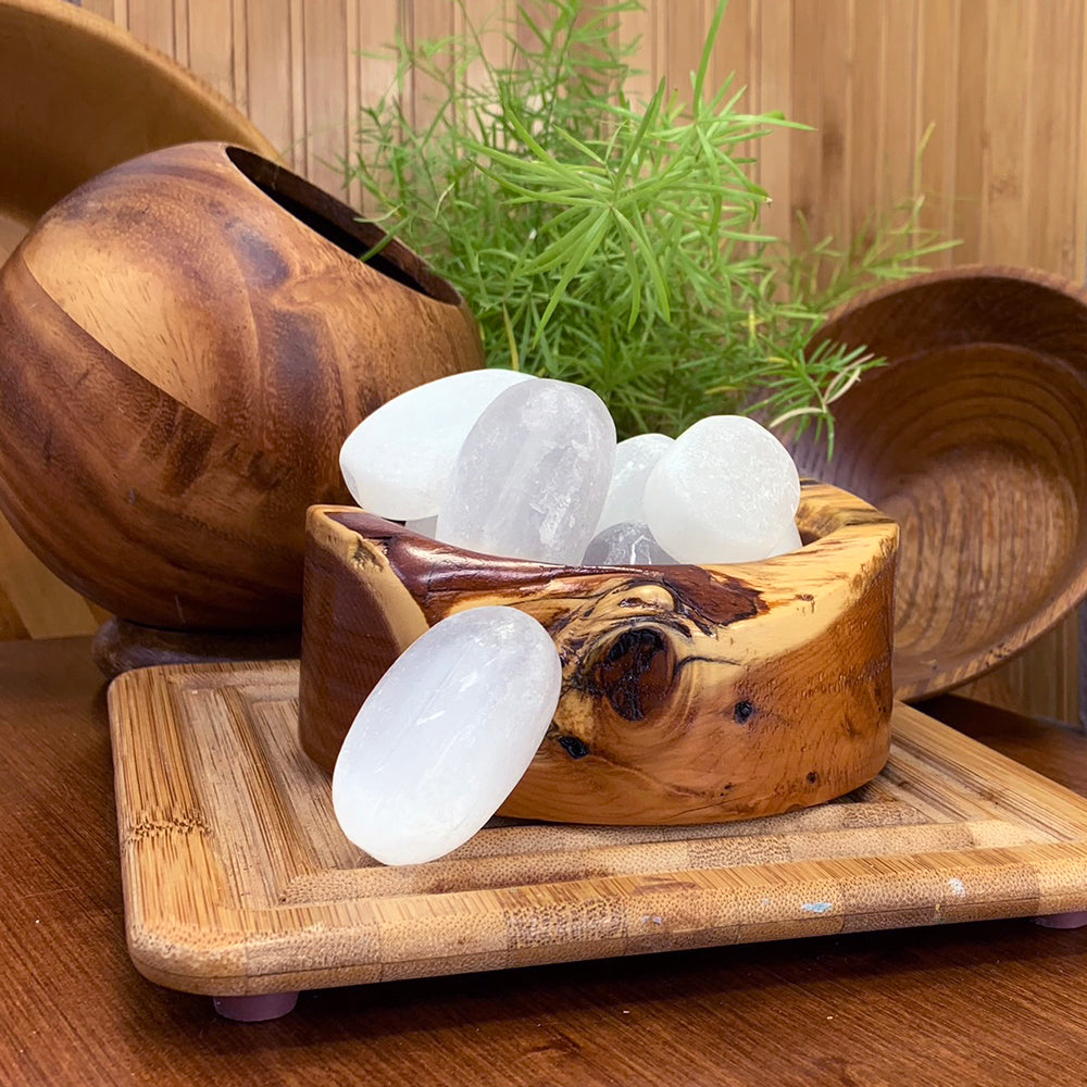 Smooth white selenite ellipse stones in a carved wooden bowl, with one resting in front on a bamboo tray