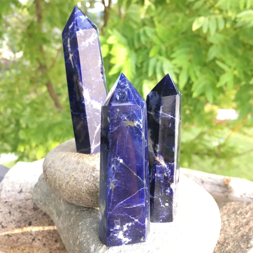 Three polished sodalite points of different heights and veining, standing on stacked river stones