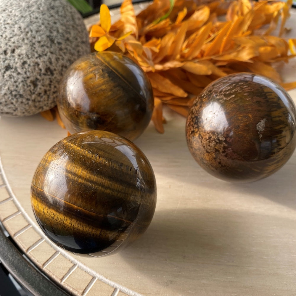 Three polished tiger's eye spheres on a table, each with different gold, brown and dark banding