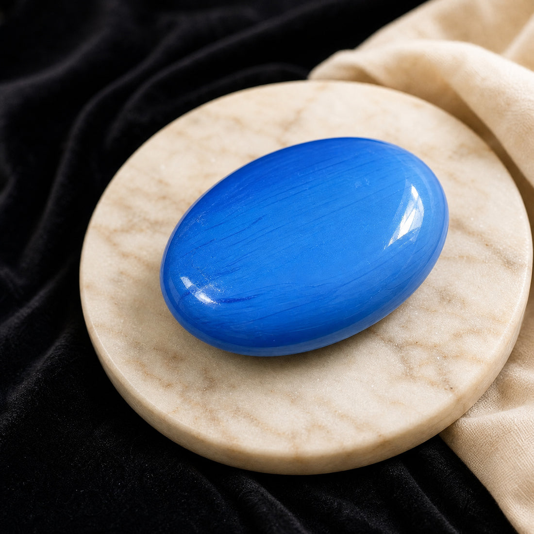 Tranquil Azure palmstone, a glossy oval of vivid blue agate with fine darker banding, resting on a marble dish