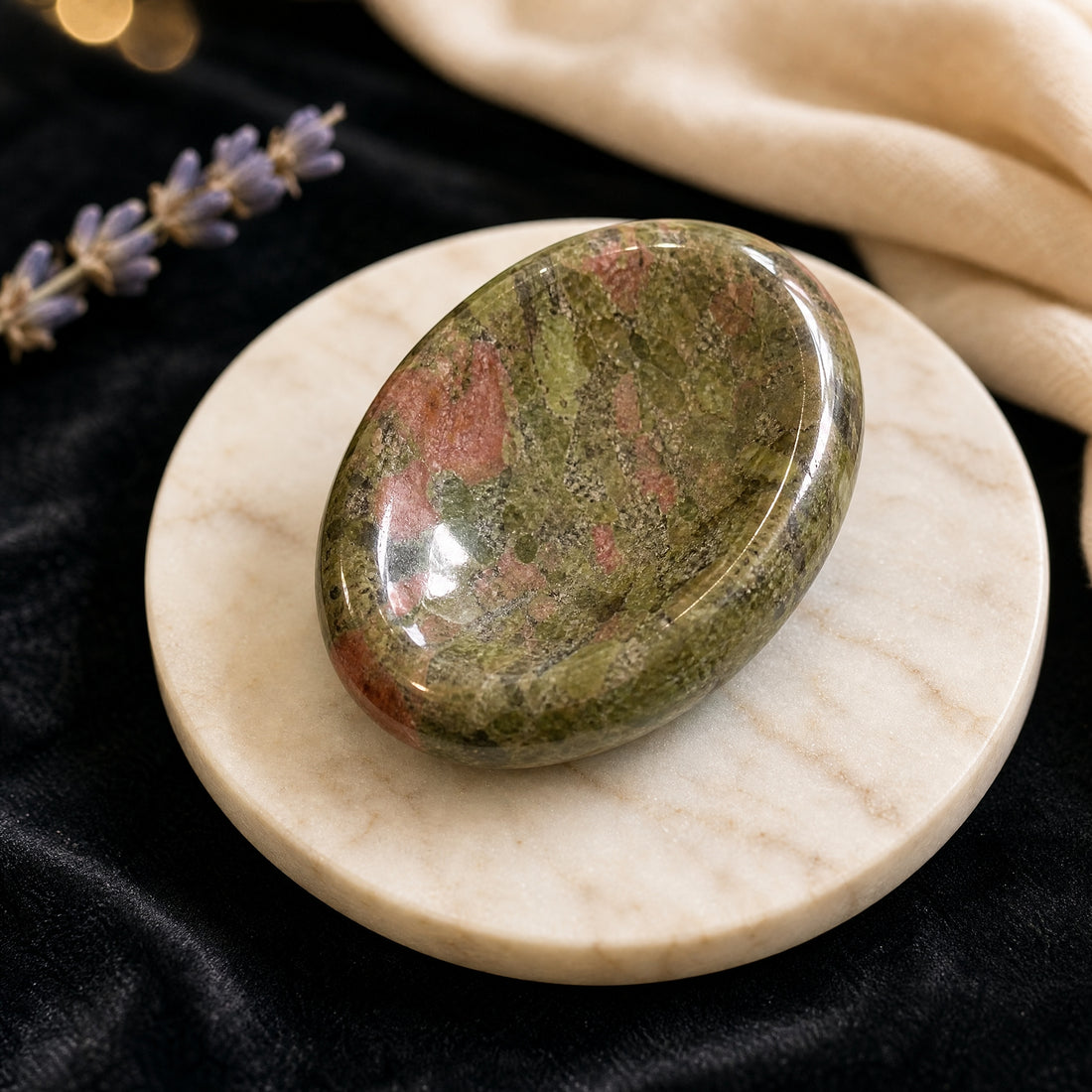 Polished unakite worry stone in mottled green and pink, its oval thumb groove facing up, on a marble coaster