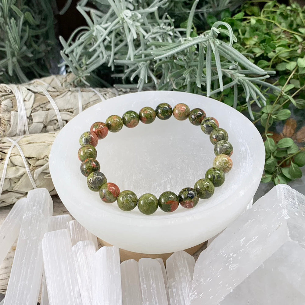One unakite mala bracelet of round green and pink beads resting in a white selenite bowl
