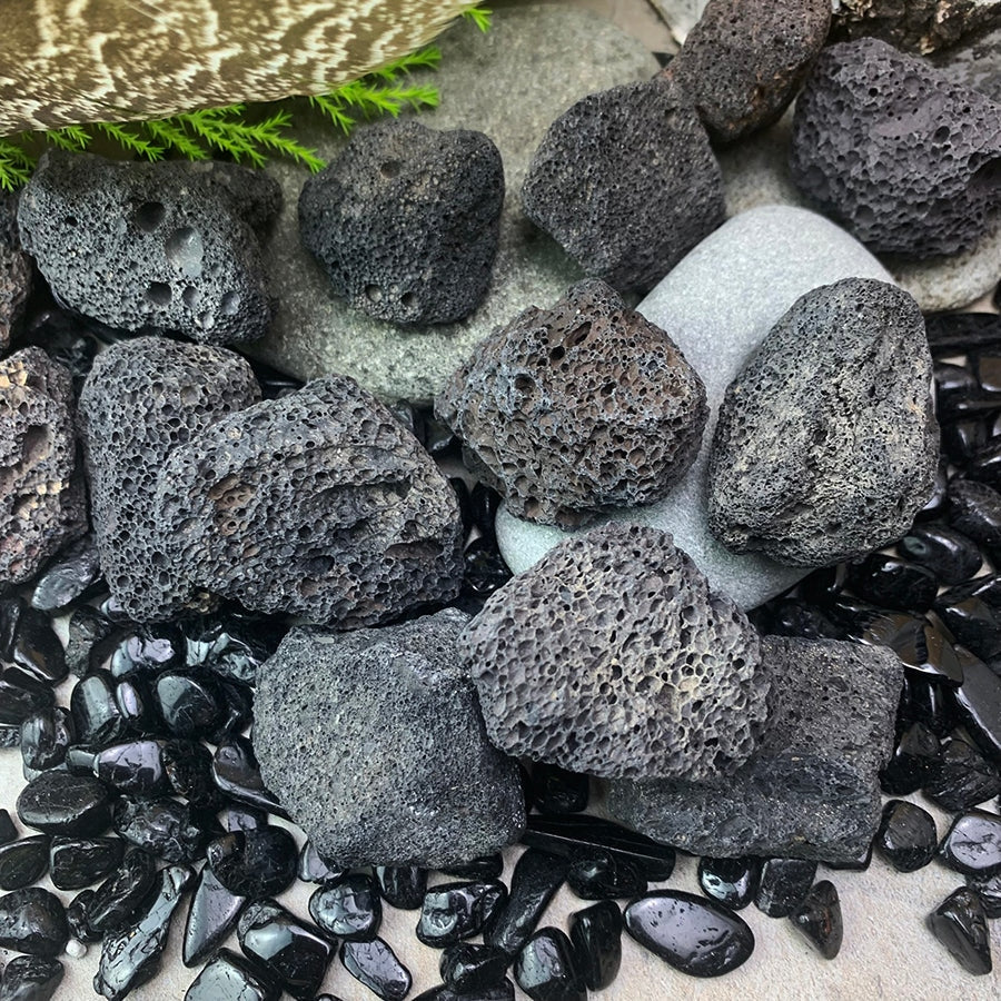 Close-up of porous black lava stones among glossy black tumbled stones and river rocks