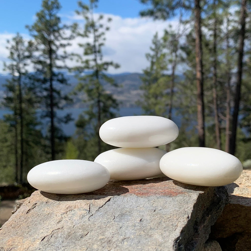 Four white quartz palmstones stacked on a granite boulder above a pine forest and lake