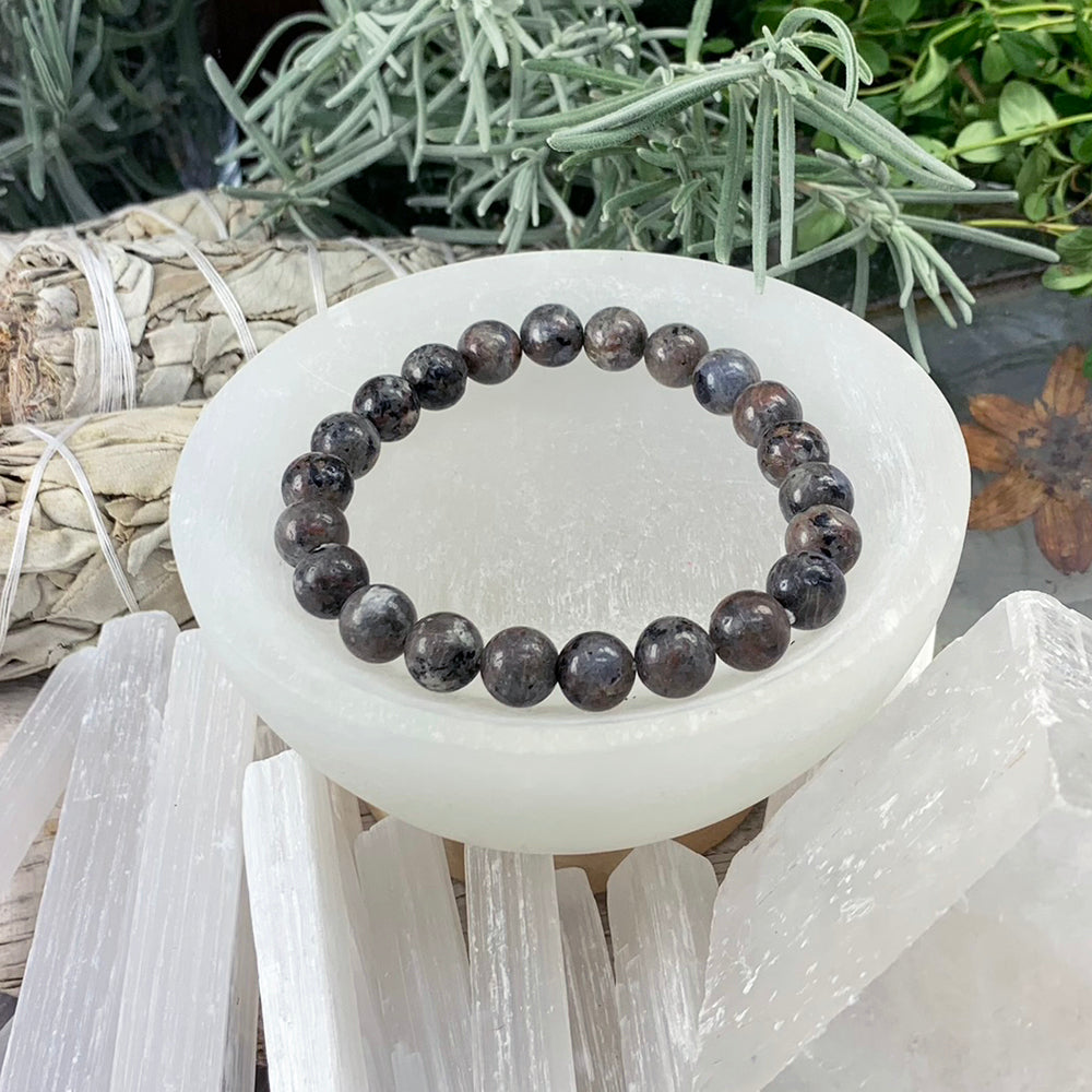 The yooperlite mala bracelet resting in a white selenite bowl, its round beads smoky grey and plum with dark flecks